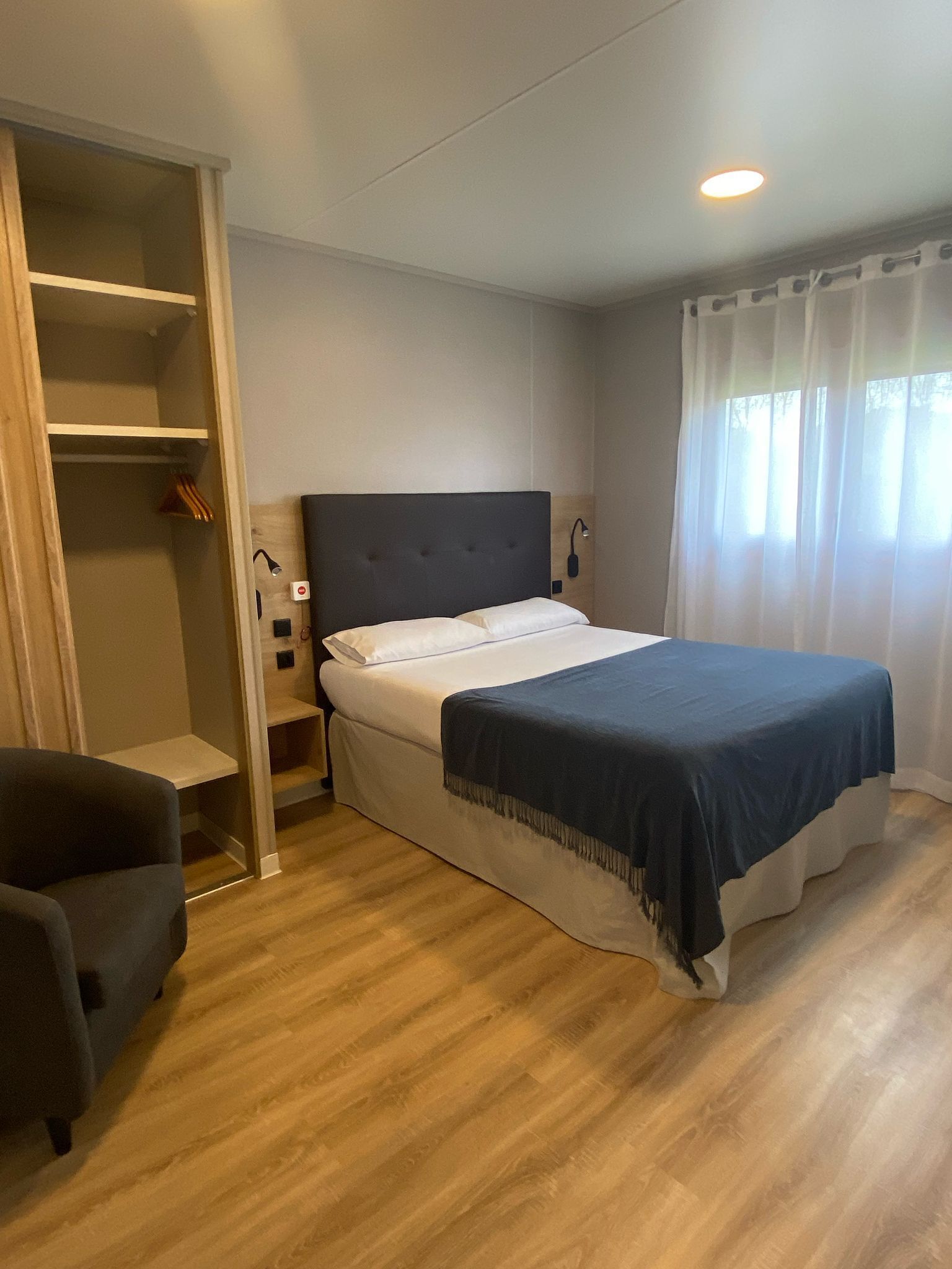Une chambre à coucher avec un lit, une armoire, une chaise et une fenêtre avec des rideaux.