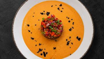 A plate with a central mound of diced vegetables on a smooth orange puree, surrounded by a white rimmed bowl on a dark surface.