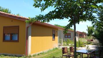 A yellow building with a tiled roof, a grassy yard, and a tree.