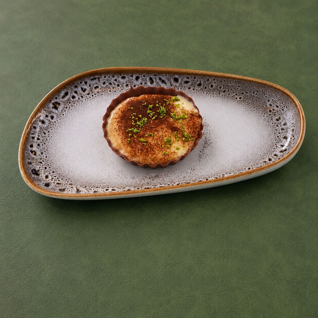 A dessert on a ceramic plate with a textured rim, placed on a green surface.