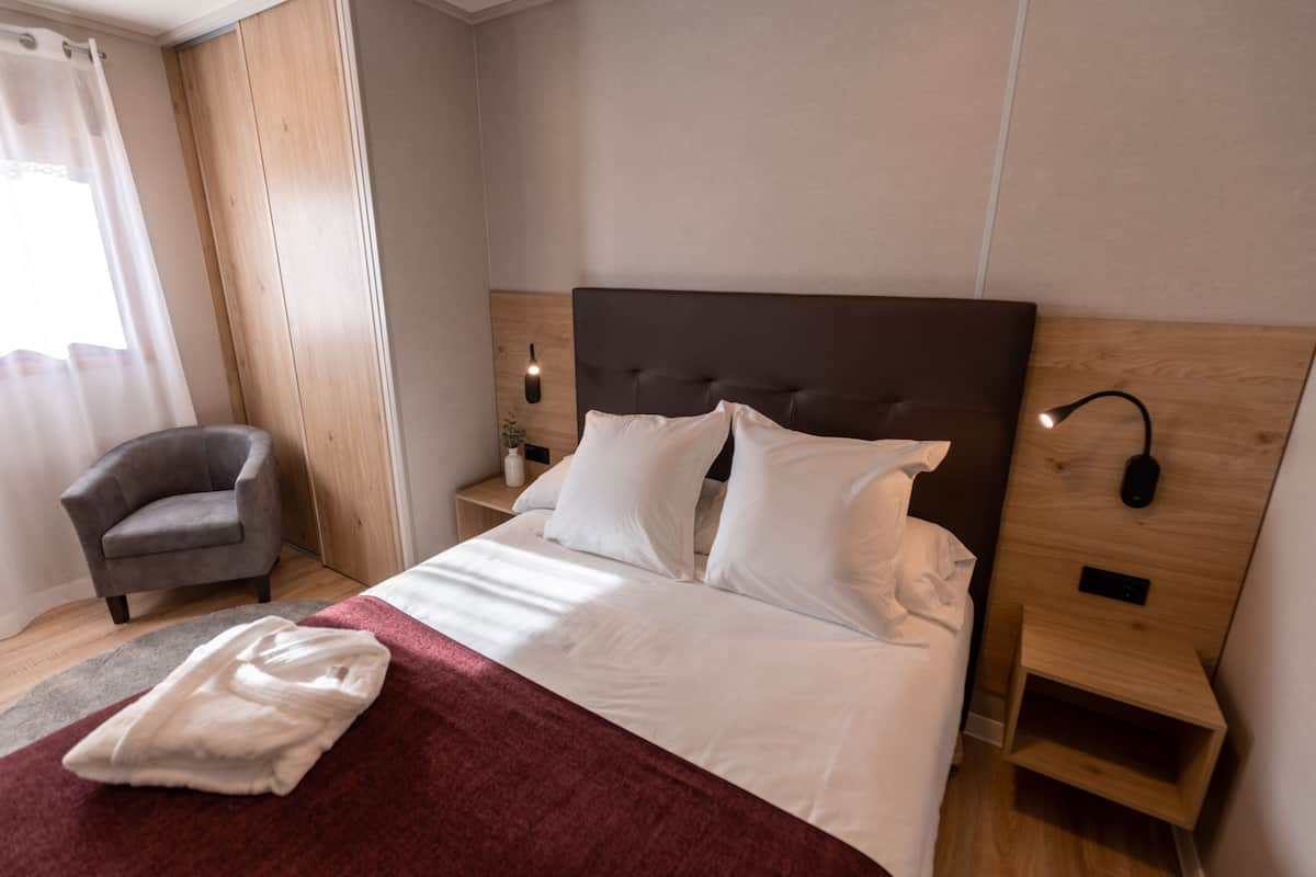 A hotel room with a large bed, a bedside table with a lamp, a chair, and a wooden headboard.