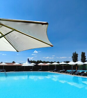 A swimming pool with lounge chairs and umbrellas, surrounded by trees and a clear sky.