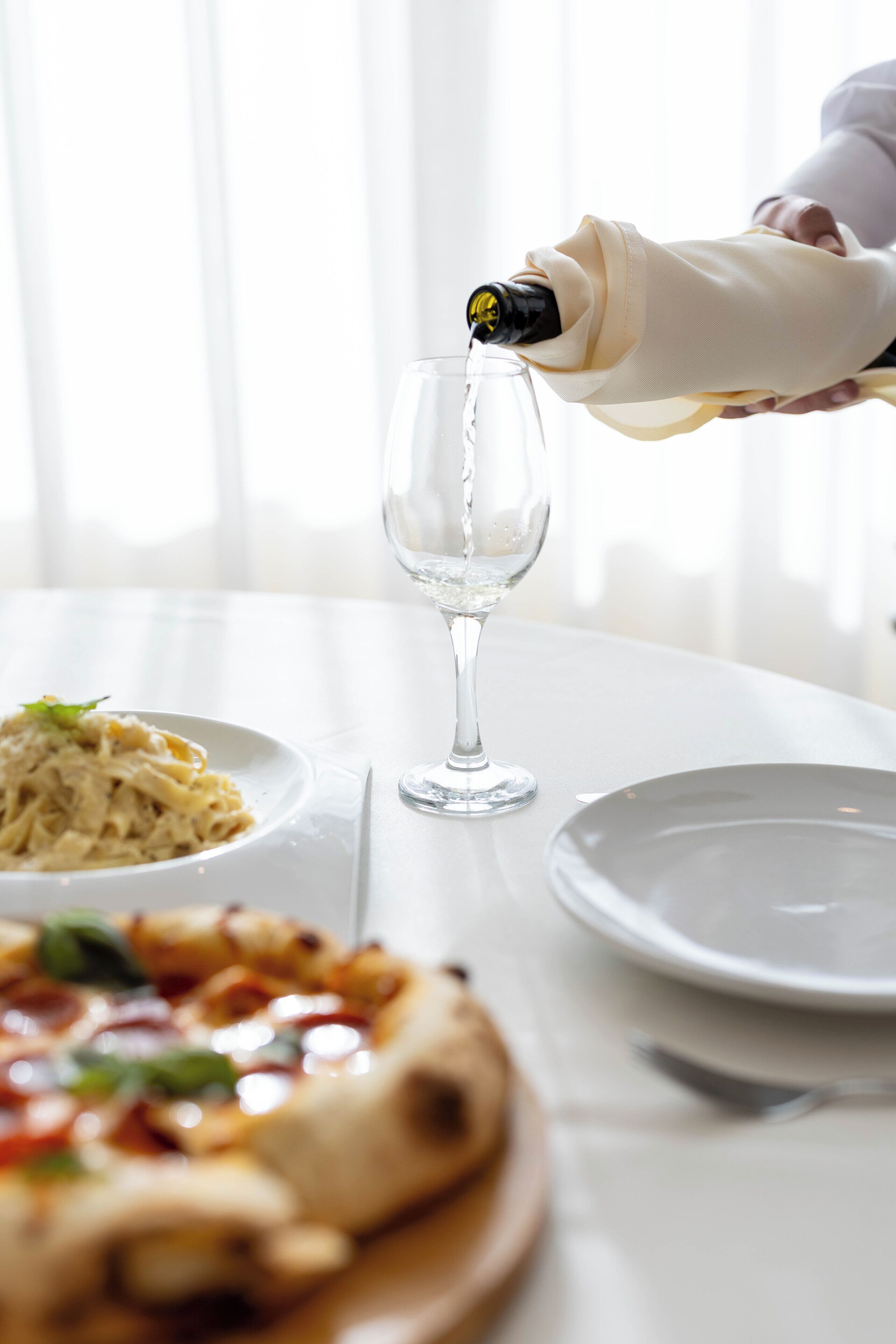 A table with a glass of water, a plate of pasta, and a pizza.