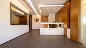 A modern hotel reception area with a marble counter, wooden paneling, and a large mirror. - Mateus hotel (Ghazir)