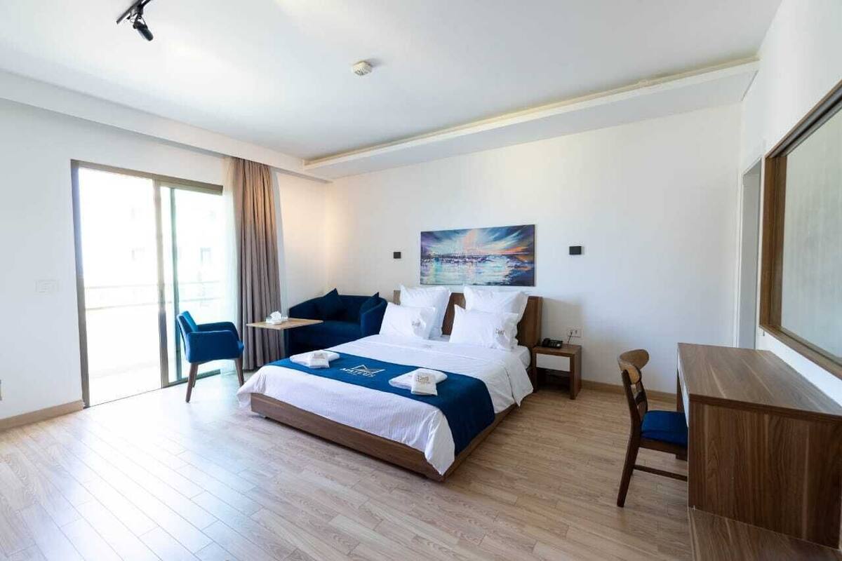 A hotel room with a large bed, a desk, a chair, and a painting on the wall.