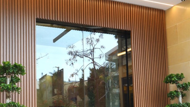 A modern building entrance with vertical wooden slats, glass doors, and potted plants. - Mateus hotel (Ghazir)
