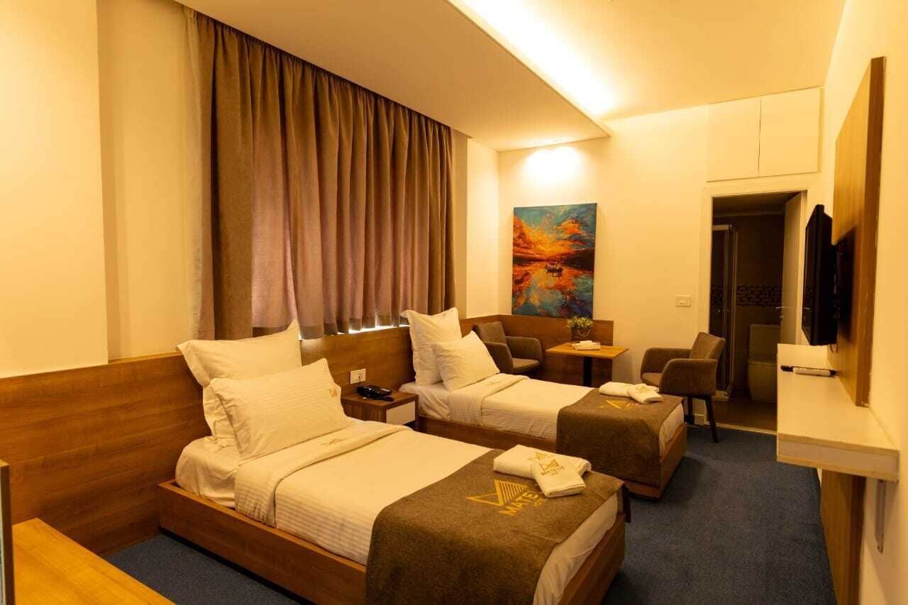 Een hotelkamer met twee bedden, een bureau, een stoel, een schilderij en een televisie.