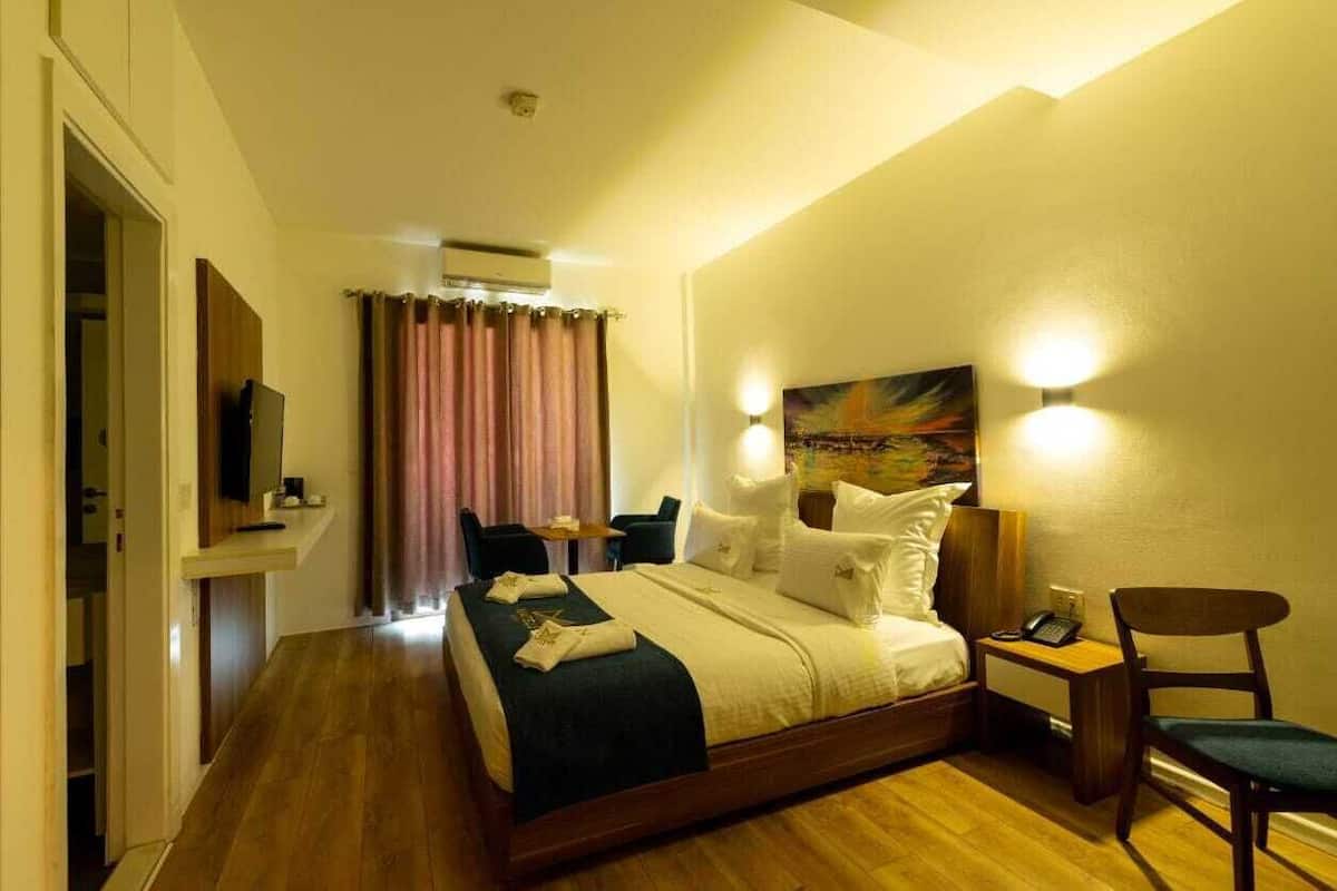 A hotel room with a bed, bedside table, chair, and a painting on the wall.