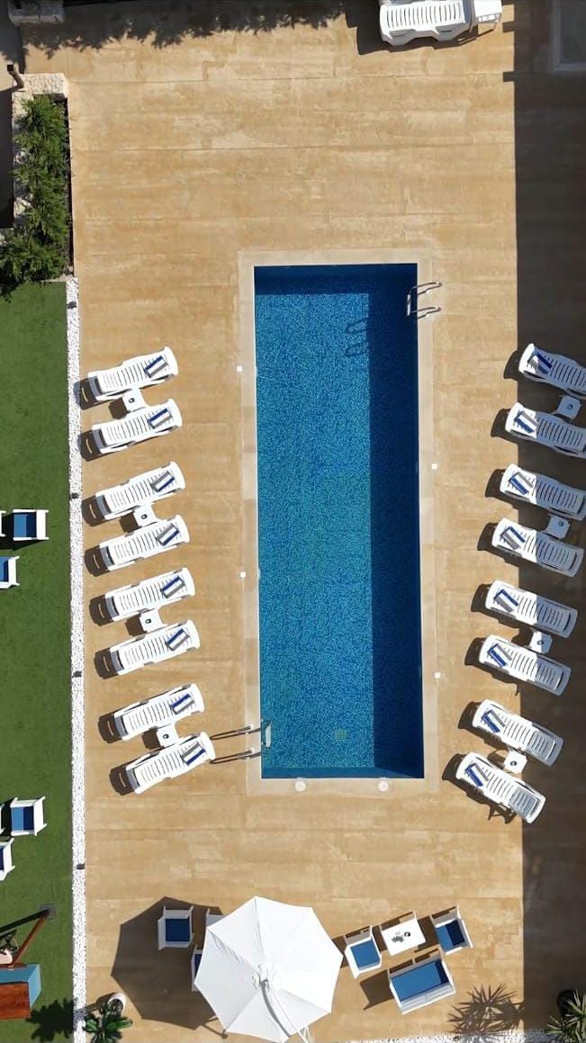 Vista aérea de una piscina con sillones de descanso y sombrillas alrededor.