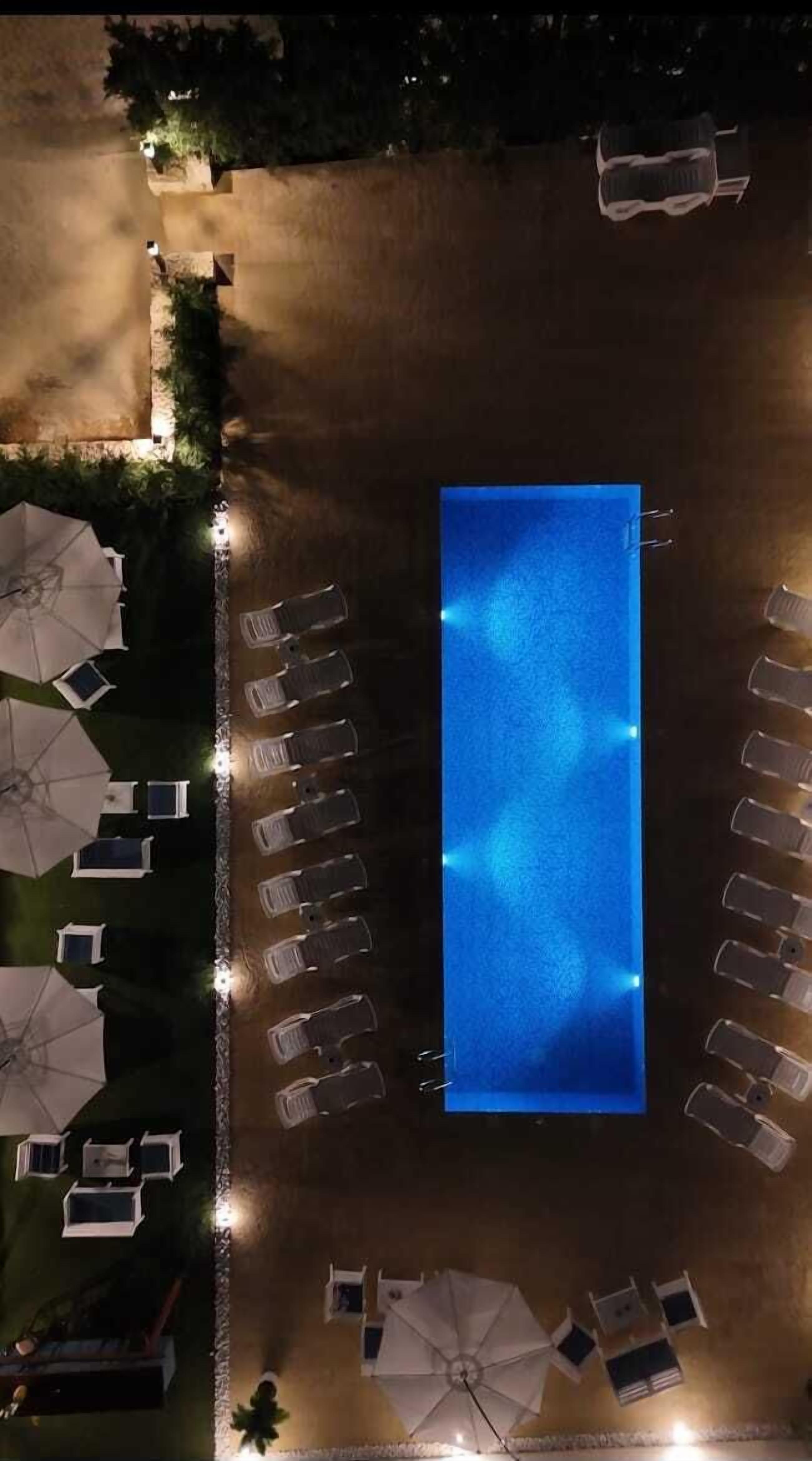 An aerial view of a swimming pool area with lounge chairs and umbrellas arranged around it.