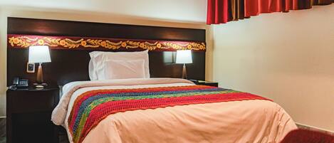 Habitación de hotel con una cama, dos lámparas de noche, un teléfono y una cortina roja.