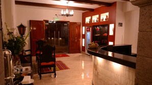 A hotel lobby with a reception desk, a red door, a chandelier, and a wall with framed pictures. - Altipacha Ayacucho Hotel (Ayacucho)