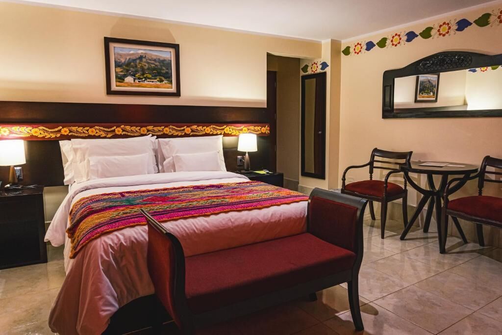 A hotel room with a bed, bedside tables, a desk with chairs, and a mirror.