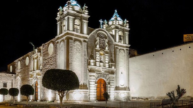 A historic church with two bell towers and a large central archway, surrounded by a low wall and a few trees. - Altipacha Ayacucho Hotel (Ayacucho)
