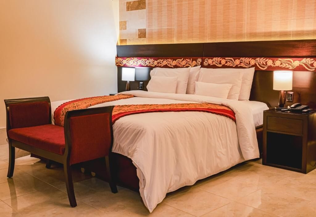 Una habitación de hotel con cama, una silla, una mesita de noche y una lámpara.
