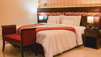 Una habitación de hotel con cama, una silla, una mesita de noche y una lámpara.
