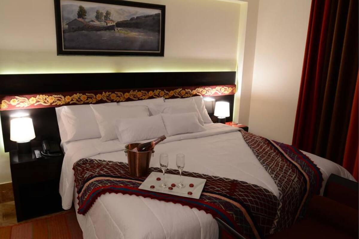 A hotel room with a large bed, two bedside lamps, a painting on the wall, and a nightstand with a phone.
