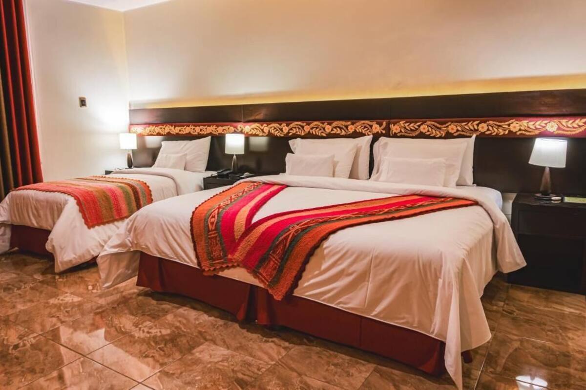 A hotel room with two beds, each with a red and white blanket, a wooden headboard, and bedside lamps.