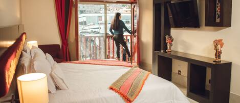 Une chambre d’hôtel avec un grand lit, un téléviseur fixé au mur et un balcon agrémenté de rideaux rouges.