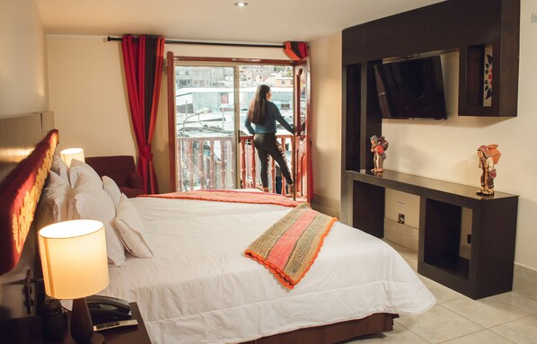 Una habitación de hotel con una cama grande, un televisor montado en la pared y un balcón con cortinas rojas.