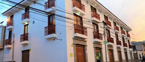 Un edificio de varios pisos con balcones, una entrada con portón y vista a la calle.