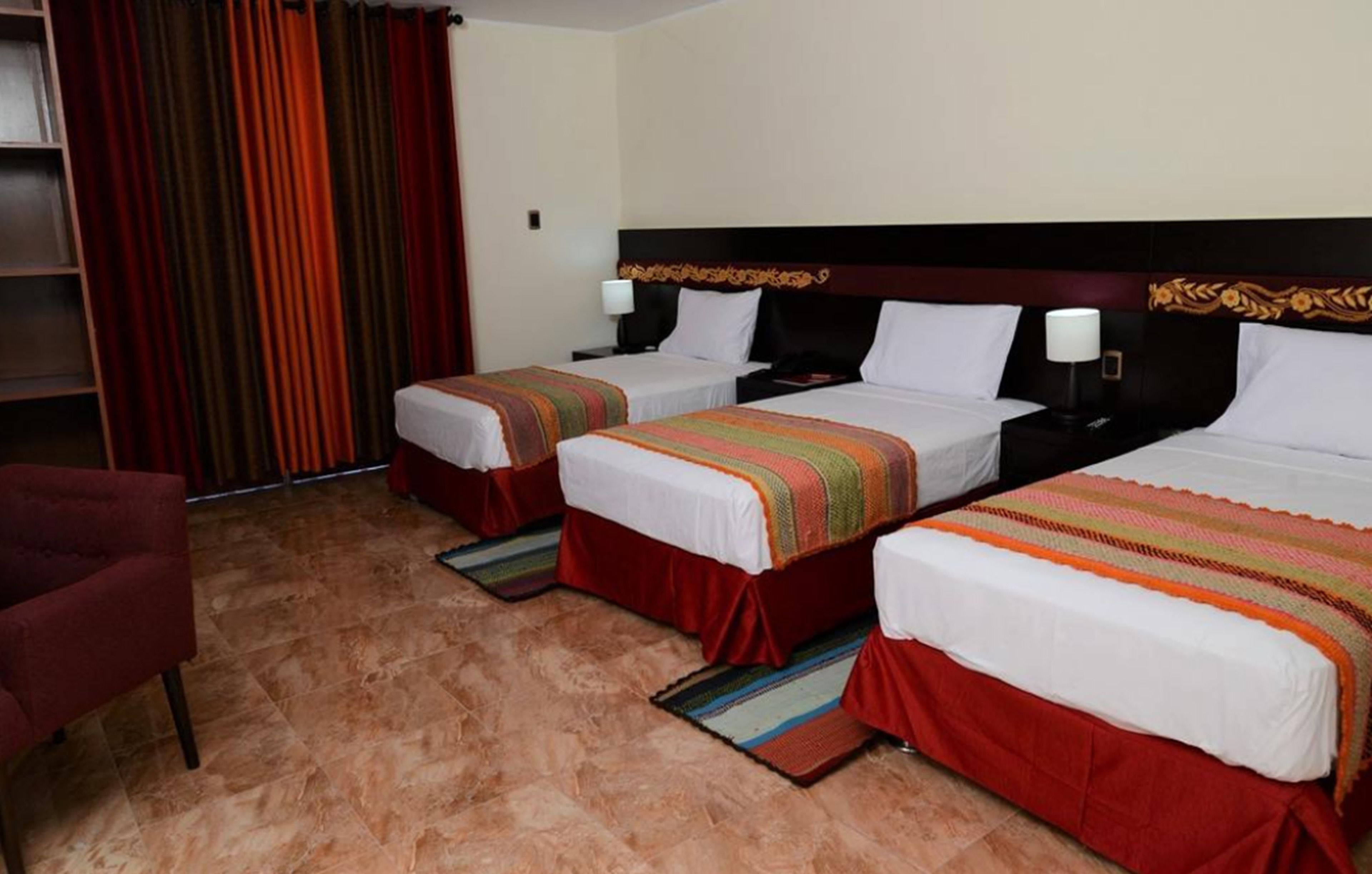 A hotel room with two beds, a red chair, and a wardrobe.