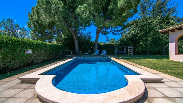 A rectangular swimming pool with a tiled edge, surrounded by a stone deck. There are two lounge chairs and a swing set in the background. -  Quiet family Villa in Pollensa countryside with pool,  just 3 km from town (pollensa)
