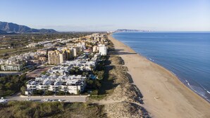 An aerial view of a coastal city with a long beach, dense residential buildings, and a clear view of the sea.