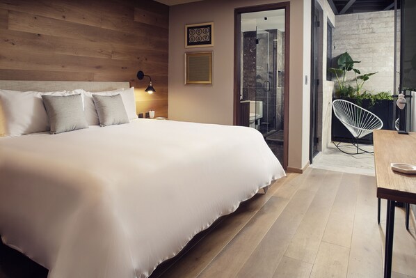 A modern bedroom with a large bed, a bedside table with a lamp, a chair, and a view of a bathroom and balcony. - Frida Boutique Stays by Viadora (Mexico City)