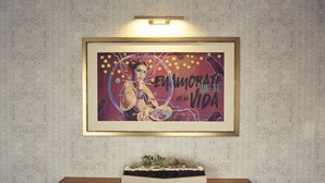 Una obra de arte enmarcada con un diseño abstracto vibrante y texto, colocada sobre una pequeña mesa con una planta.