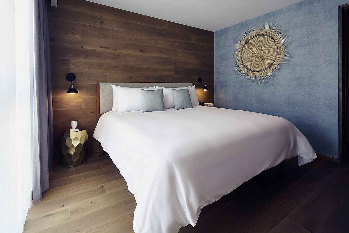 Un dormitorio moderno con cabecera de madera, una cama grande con ropa blanca, dos lámparas de noche y un adorno de pared.