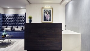 Un área de recepción moderna con un mostrador de madera oscura, una obra de arte enmarcada encima y un sofá tapizado en azul con cojines al fondo.