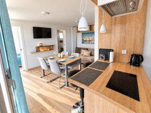 A modern kitchen with a built-in stove, a dining area with a wooden table and chairs, and a living area with a sofa and a painting.