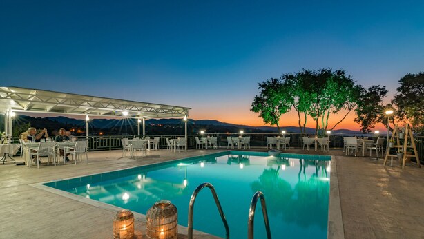 Un espace aménagé au bord de la piscine, offrant une vue sur le coucher de soleil, avec des tables, des chaises et un coin salon abrité.