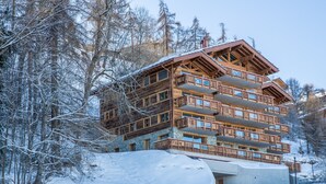 A multi-story wooden lodge with balconies, surrounded by snow-covered trees. - La Forêt 2 - Spa access (Haute-Nendaz)