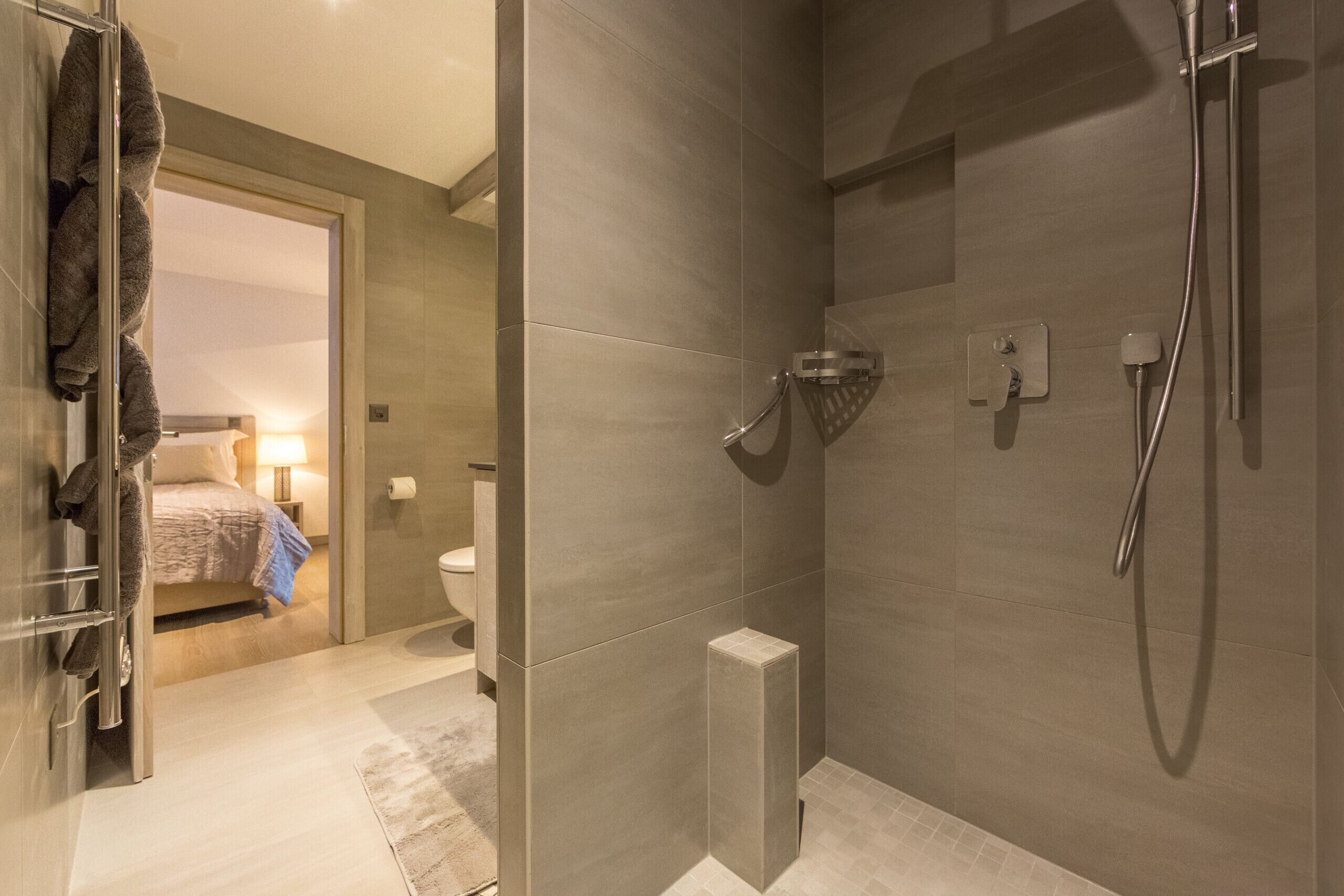 Een moderne badkamer met douche, toilet en een zichtbaar bed in de aangrenzende kamer.