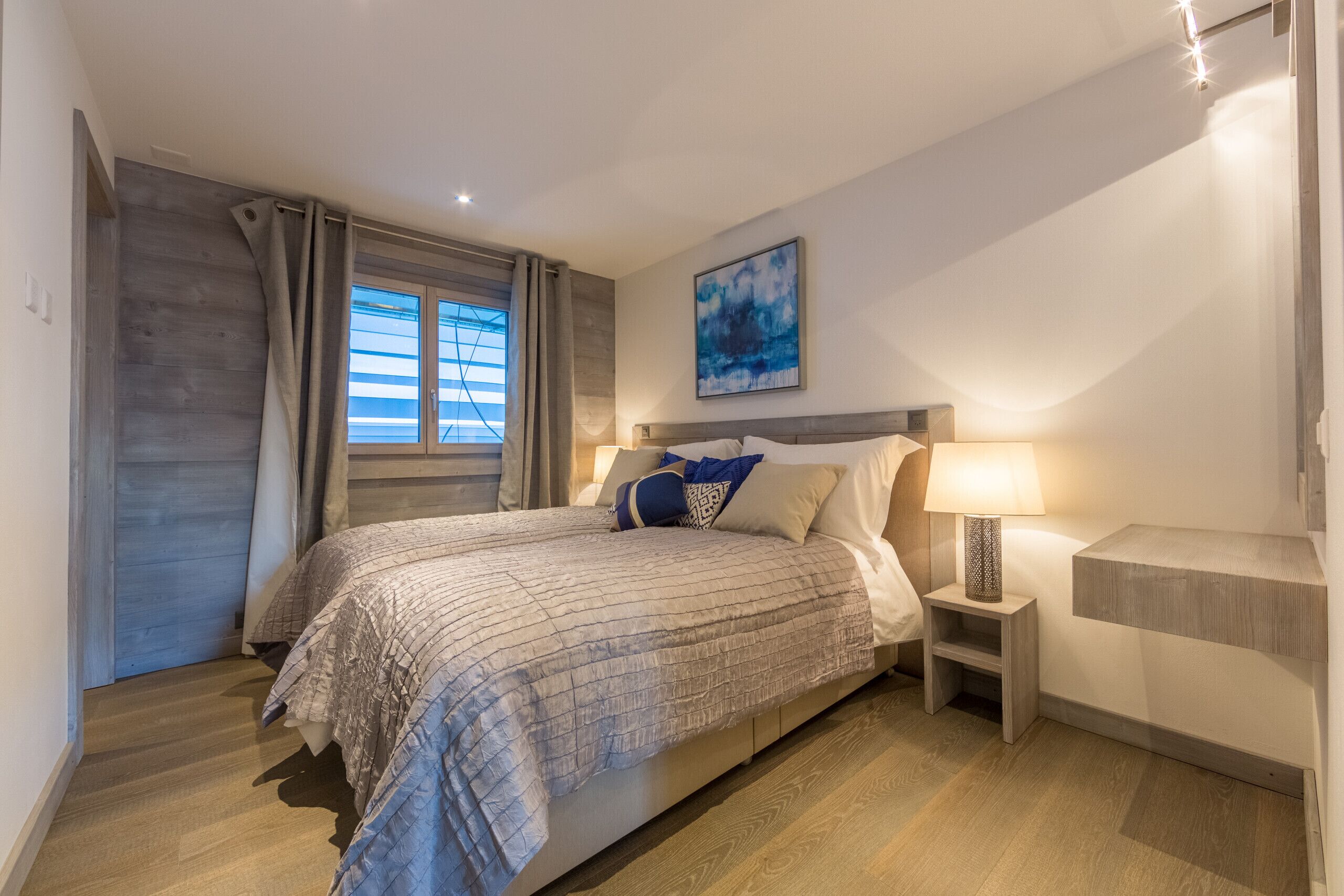 Une chambre à coucher avec un lit, des tables de chevet, une lampe et un tableau au mur.