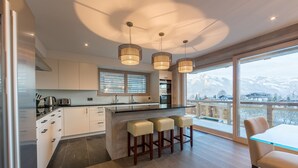 A modern kitchen with a large island, bar stools, and a view of mountains. - La Forêt 2 - Spa access (Haute-Nendaz)