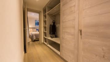 Un pasillo con un armario de madera, una cama con cabecera azul y un aspirador en un estante.