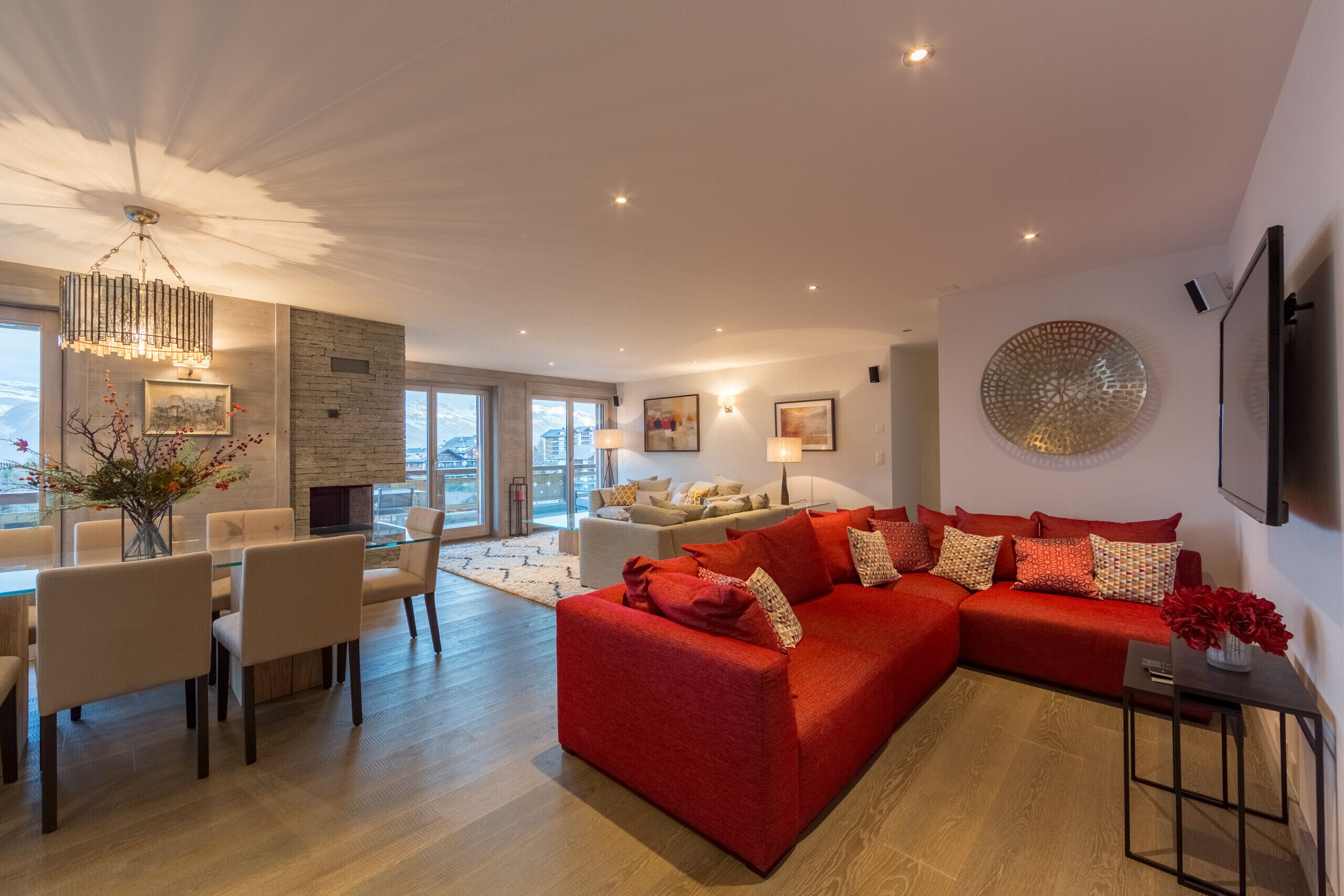 A modern living room with a red sofa, a dining area with a glass table, and a fireplace.