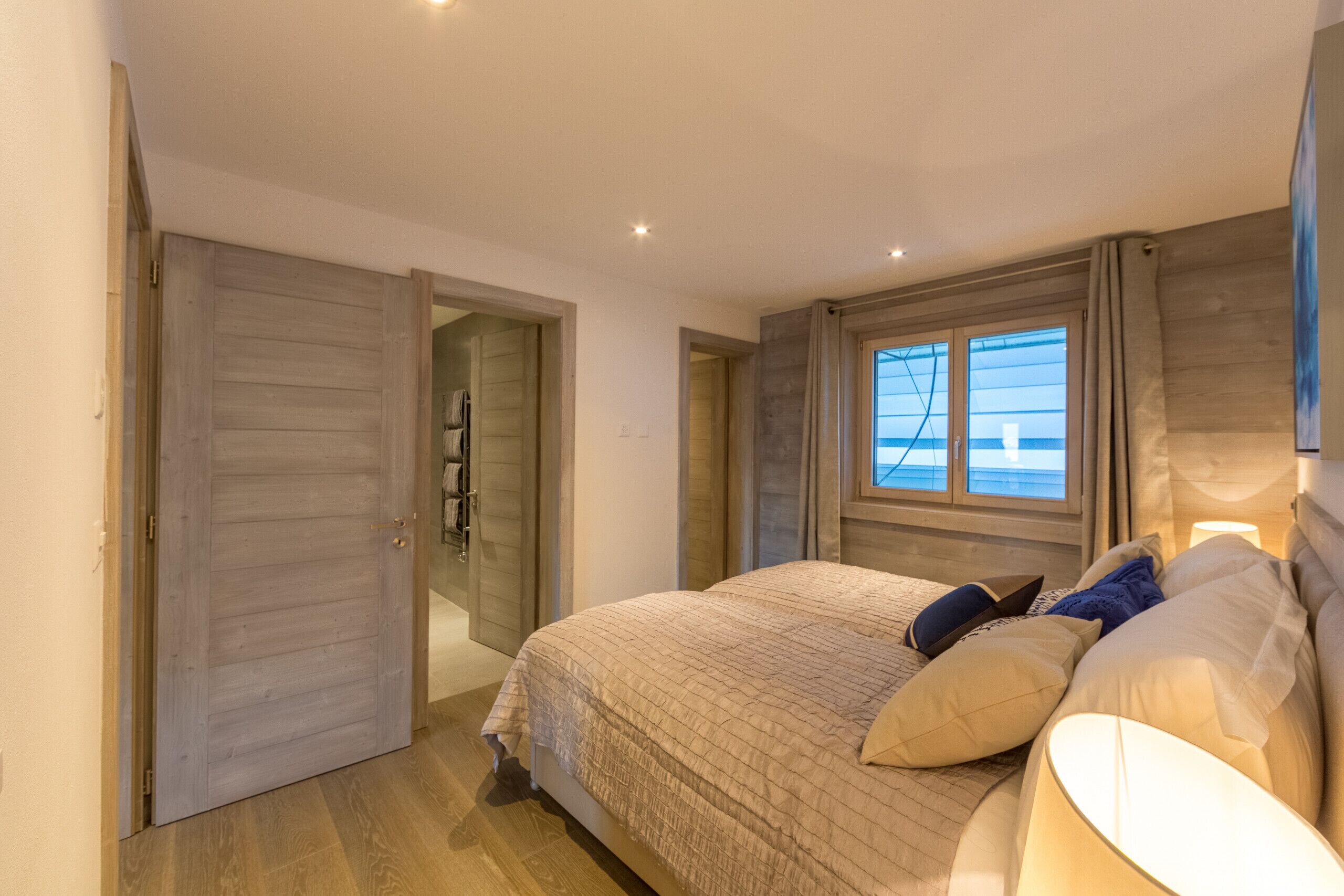 Une chambre à coucher comprenant un lit, une table de chevet, une fenêtre avec des rideaux et une porte donnant sur une autre pièce.