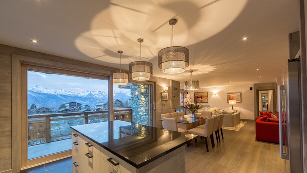 A modern kitchen with a large island, pendant lights, and a view of snow-capped mountains. - La Forêt 2 - Spa access (Haute-Nendaz)