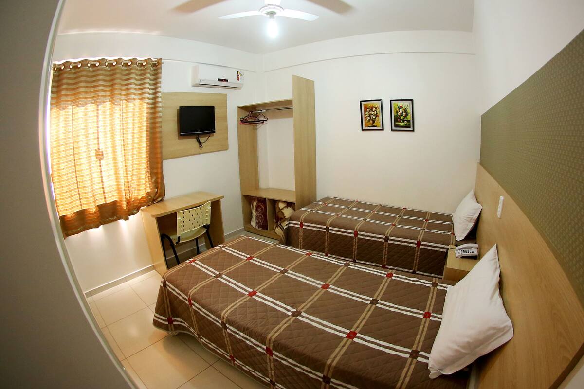A bedroom with two beds, a desk, a TV, and a wardrobe.