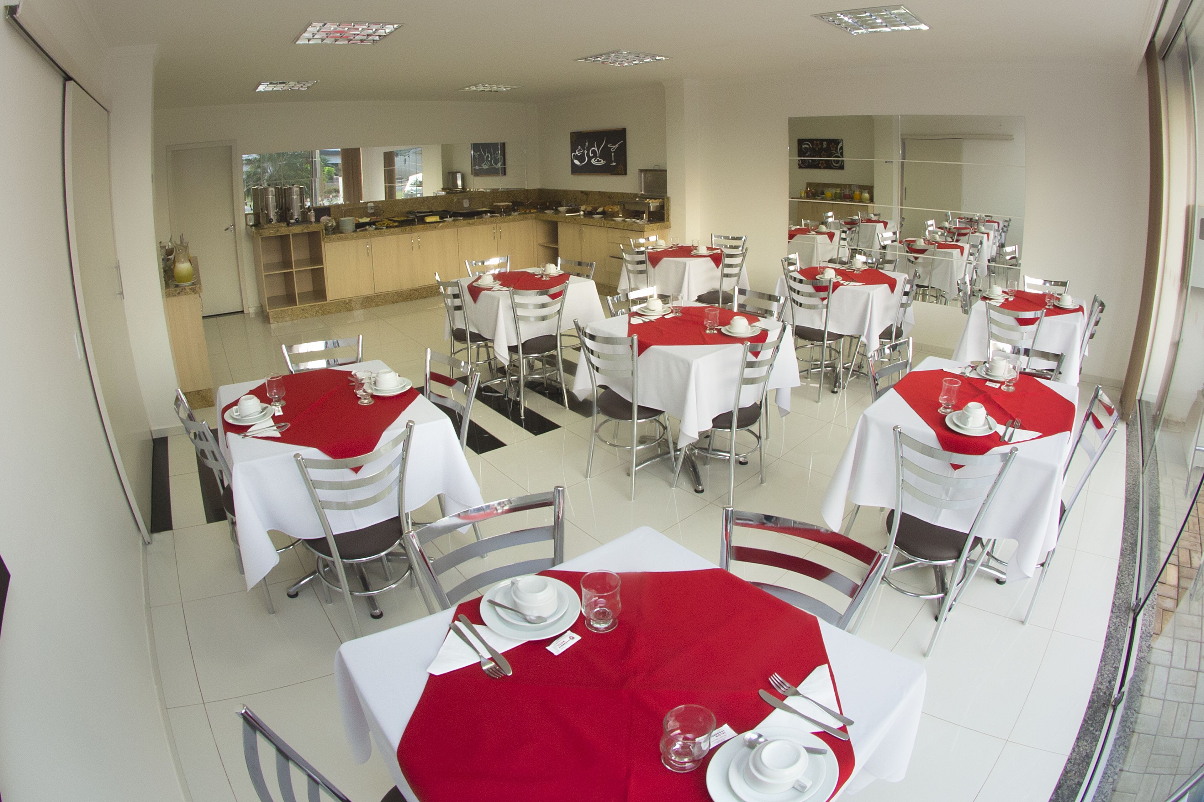 A restaurant with multiple tables set for dining, featuring white tablecloths and red accents.