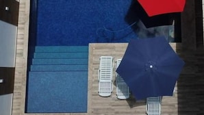 Une piscine avec une terrasse en bois, deux chaises longues blanches et deux parasols.