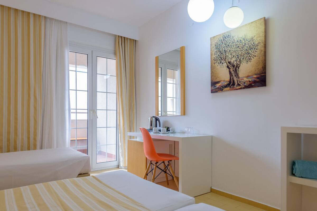 A hotel room with two beds, a desk, a chair, a painting, and a window with curtains.