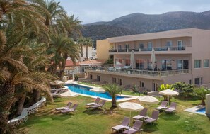 Un hotel con piscina, sillones de descanso y palmeras.