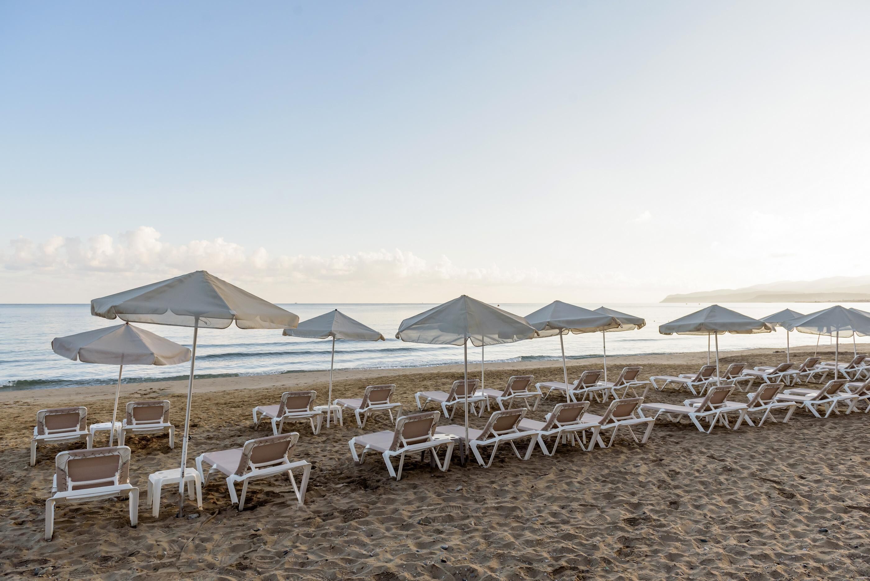 A beach with rows of white lounge chairs and umbrellas.