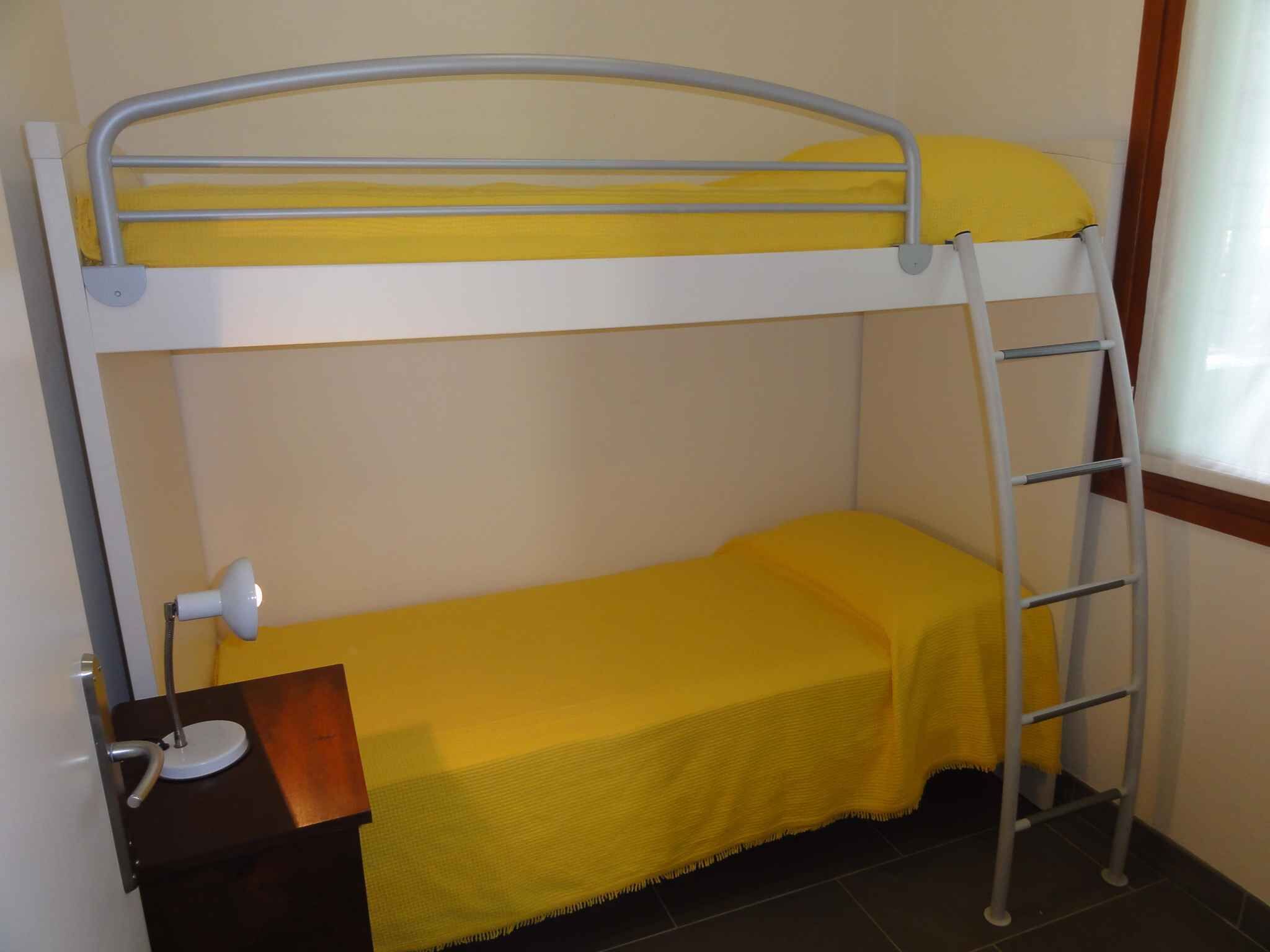 A bunk bed with a ladder, a desk with a lamp, and a window with curtains.