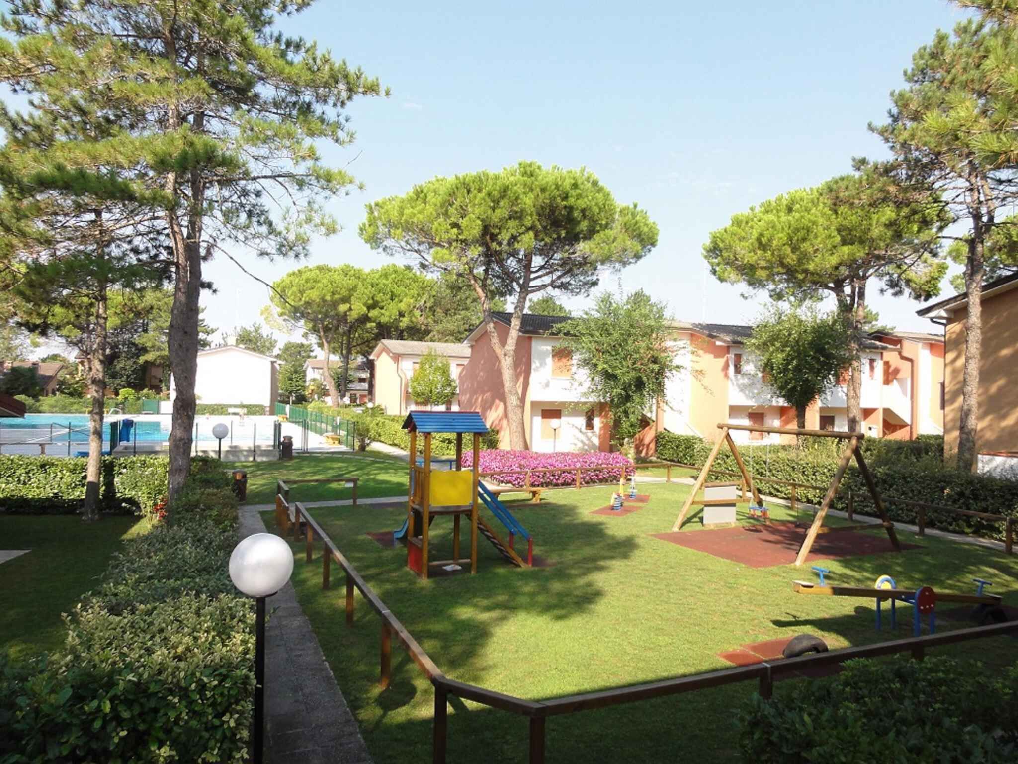A playground with a slide, swing set, and climbing structure, surrounded by well-maintained grass and trees.
